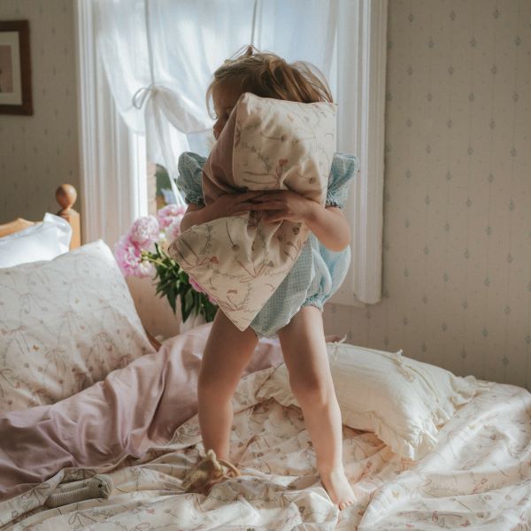 Bows & Butterfly Kisses Toddler Pillow in Pink. Child is standing on top of bed hugging the pillow.