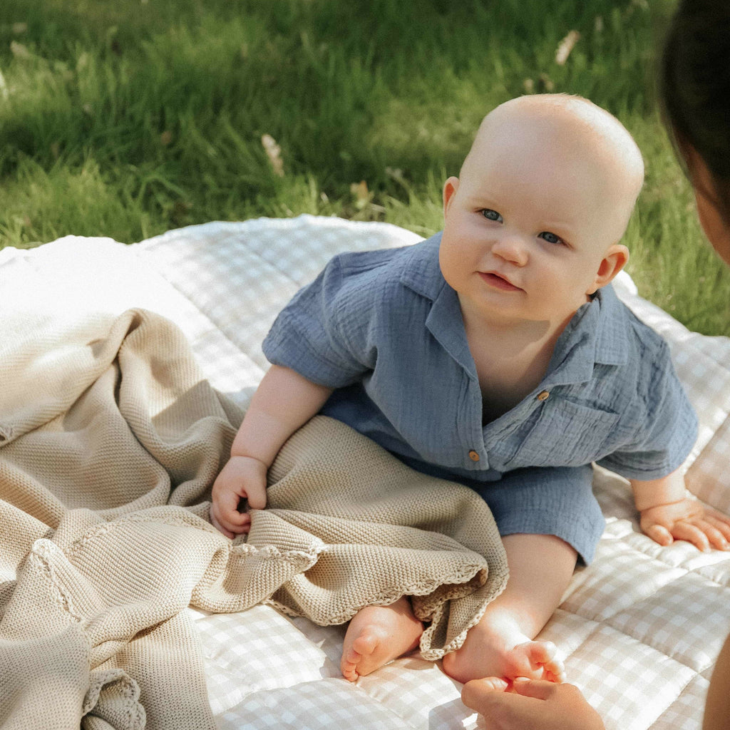 Baby sitting on gingham picnic blanket with knit beige blanket